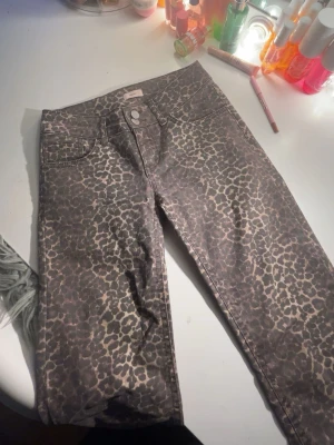 Leopardmönstrade jeans från Nelly - Säljer ett par snygga jeans från Nelly med leopardmönster i bruna och beige toner. Byxorna har klassisk femficksmodell, knapp och dragkedja framtill samt raka ben. Materialet är mjukt och stretchigt för skön passform.