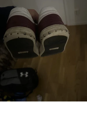 Vinröda sneakers med vit detalj - Snygga vinröda sneakers med vit rand på sidan och matchande vita detaljer vid häl och sula. Skorna har klassisk snörning och rund tå. Perfekta för dig som gillar en stilren men ändå färgstark look.