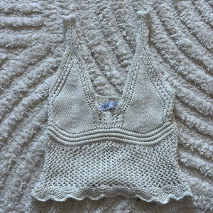 Stickad linnetopp från Zara i beige - Superfin stickad linnetopp från Zara i creamfärg med v-ringning och breda axelband. Toppen har virkad känsla, vågig kant nertill och är perfekt för varma dagar. Snygg att styla med jeans eller kjol för en chill look.