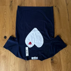 Mörkblå Comme des Garçons Play t-shirt - Snygg mörkblå t-shirt från Comme des Garçons Play med stort vitt hjärta och röd logga med ögon på bröstet. Klassisk passform och korta ärmar, tillverkad i mjuk bomull. Aldrig använd och är i storlek L men passar även dem som har storlek M