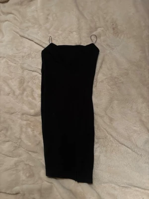 Svart axelbandslös kort klänning - Säljer en svart, tight och axelbandslös kort klänning med smala axelband. Klänningen har en enkel och stilren design som passar perfekt till olika tillfällen. Materialet känns mjukt och följsamt mot kroppen.