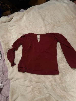 Mörkröd långärmad topp med v-ringning - Snygg mörkröd topp med långa ärmar och v-ringad öppning framtill. Perfekt för dig som gillar stilrena plagg med en twist. Passar till både jeans och kjol för en trendig look.
