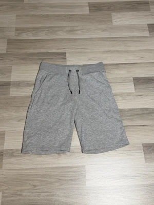Grå mjukisshorts från peak performamce  - Snygga grå mjukisshorts i bomull med elastisk midja och snörning framtill. Shortsen har två sidofickor och en bakficka, perfekt för en avslappnad och sportig stil. Passar dig som gillar bekväma och stilrena plagg.