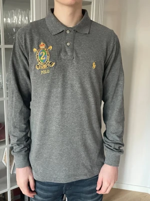 Grå långärmad pikétröja från Polo Ralph Lauren - M - Jag säljer den här riktigt snygga långärmade pikétröjan från Polo Ralph Lauren i storlek M. Den är i fint skick utan skador och defekter. Nypris ligger på 2000kr och jag säljer den här för 399kr. Tveka inte att höra av er!