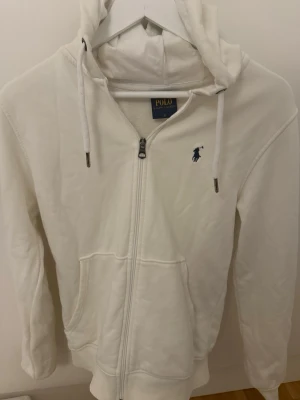 Vit ziphoodie från Polo Ralph Lauren kom med annat prisförslag - Säljer en stilren vit hoodie från Polo Ralph Lauren med dragkedja framtill och två fickor. Skicket 8/10 och nypris 1600 