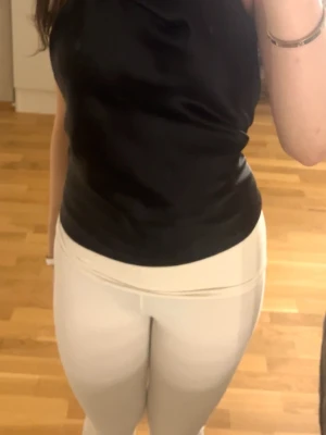 Svart satinlinnetopp med öppen  - Snygg svart linnetopp i satin med öppen rygg och slät finish. Toppen har en figurnära passform och är ärmlös, perfekt för att styla med både jeans och kjol. Materialet ger en lyxig känsla och glans.