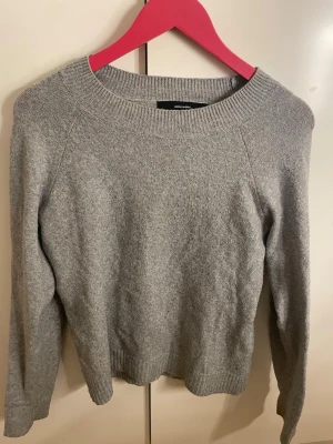 Grå stickad tröja från Vero Moda - En enkel och stilren grå stickad tröja från Vero Moda. Tröjan har rund halsringning, långa ärmar och ribbade muddar vid ärmslut och nederkant. Perfekt basplagg till garderoben och lätt att matcha med olika outfits.
