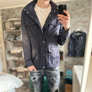 Mörkblå vindjacka med fickor - Mycket bra skick, inga defekter! Storlek M sitter som M  och passar dig som är mellan 180-190cm ungefär. Nypris ca 1500kr. Modellen är 185 cm, 75kg. Passar bra nu till våren! Skriv för mer information!