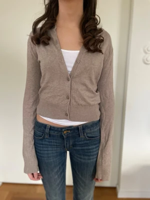 Beige kofta med knappar från hm - Snygg beige cropped kofta med långa ärmar och knäppning framtill. Koftan har en enkel, stilren design och är gjord i ett tunt, mjukt material som passar perfekt till jeans eller kjol. Perfekt för lager på lager och en avslappnad look. Jättefin och passar till allt. Inga noppror, hål eller fläckar för endast använd en gång men harlite defekter från tvätt. Storlek xs