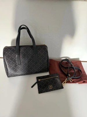 Väska  - Snygg svart handväska från Malene Birger med diskret rutigt mönster och guldfärgade detaljer. Väskan har två handtag, avtagbar axelrem och matchande liten plånbok med dragkedja. Perfekt för dig som gillar stilrena accessoarer.