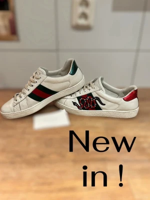 Gucci Ace sneakers med orm - Gucci Ace sneakers i vitt skinn med klassiska gröna och röda ränder på sidan och broderad orm. Metallic-detaljer i rött och grönt på hälen, samt snörning framtill. Snygg och ikonisk modell som sticker ut med sina detaljer. Har inte tvättat dom jätte noggrant och orginal sula gick sönder men man får med en Vagabond sula som passar bra. Dom Svåra att hitta dom kostar runt 9000 tusen och jag säljer dom för 2099 passa på att köp pris är inte hugget i sten! Hör av dig vid minsta lilla fundering!😀