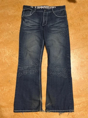 Blå bootcut jeans med detaljer - Snygga blå bootcut jeans med ljusa slitningar och dekorativa nitar på låren och knäna. Snygg boot cut/flare. Alla detaljer är embroidered. Mått: midja: 44cm längd: 105cm benöppning: 27cm. Skriv vid frågor/ köp!