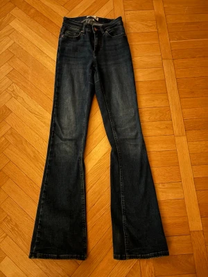 Mörkblå bootcut jeans med medel hög midja - Snygga mörkblå bootcut jeans med medel hög midja och klassisk femficksdesign. Jeansen har en lätt tvättad look och är tillverkade i ett mjukt denimtyg som ger en skön passform🩷