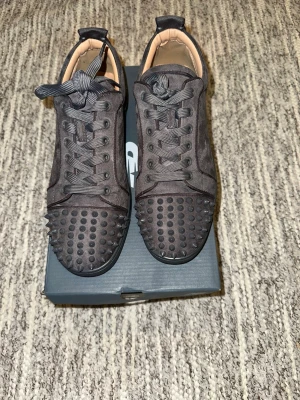 Christian louboutins  - Säljer ett par svarta sneakers från Christian Louboutin i mocka med coola nitar på tån och sidorna. Skorna har snörning och den klassiska röda sulan. Perfekta för dig som vill sticka ut med en edgy stil.