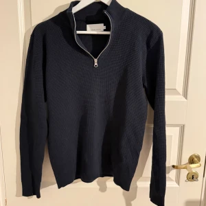 Mörkblå halvzip tröja Casual Friday - Mörkblå stickad tröja från Casual Friday med halvzip och hög krage. Tröjan har en grovstickad struktur och långa ärmar, perfekt för lager på lager. Enkel men stilren design som passar till det mesta. Passar S 