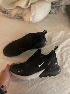 Nike 270 svarta sneakers - Säljer mina Nike  270 sneakers i svart med vita detaljer och rött undertill. Dom är väl använda med 2 hål på båda sidorna av skorna där av priset annars inget fel på dom:)