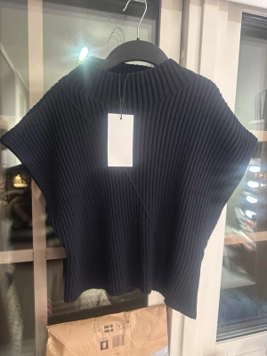 Svart ribbad stickad topp från Zara - Säljer en svart ribbad stickad topp från Zara. Toppen har korta ärmar, hög hals och är gjord i ett mjukt, stretchigt material. Perfekt att styla med jeans eller kjol för en trendig look.