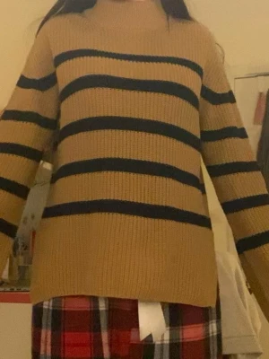 Brunstickad tröja med svarta ränder - Säljer en brun stickad tröja med breda svarta horisontella ränder. Tröjan har en rak passform, liten slit vid båda sidorna, och långa ärmar. Perfekt för dig som gillar en enkel men snygg stil till hösten eller vintern.