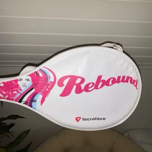 Tecnifibre Rebound Tennisträningsracket- barn - Tecnifibre Rebound tennisträningsracket i vitt och rosa. Racketen levereras med skyddande fodral med dragkedja och axelrem. Handtaget är lindat med beige grepptejp.   -Ca 65 cm långt - sliten handtag men fortfarande helt fungerande (visas i bild)