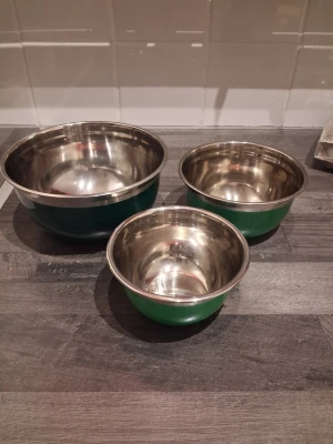 Tre gröna metallskålar - Säljer ett set med tre skålar med grön utsida. Perfekta för matlagning, bakning eller servering. Bunkarna är runda och har en blank insida i metall. Snygg och enkel design som passar i alla kök.                                                                          Stor skål ca 18cm i diameter och ca 9cm hög.        Mellan ca 14.5cm i diameter ca 7cm höga.              Liten ca 12cm i diameter och 6cm hög 