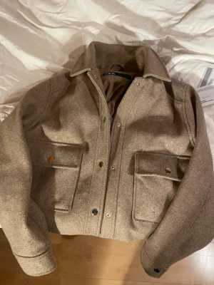 Beige jacka från Zara - Stilren beige overshirt från Zara i ullmix med klassisk krage, stora fickor framtill och knappstängning. Perfekt för lager på lager och ger en clean look till din outfit. Ställ gärna frågor! Exempel om mer bilder😊