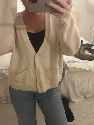 & other stories kofta - Mysig beige stickad kofta med v-ringning och tre knappar framtill. Koftan har två framfickor och ribbade muddar vid ärmslut och nederkant. Perfekt att slänga över en topp för en avslappnad look.