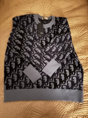 Mörkblå stickad tröja från Dior - Snygg mörkblå stickad tröja från Dior med ikoniskt monogrammönster i grått och svart. Tröjan har rund halsringning, ribbade muddar och nederkant samt en exklusiv känsla.