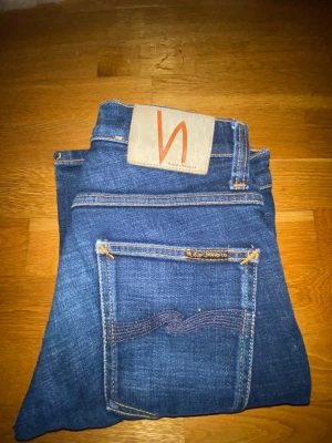 Nudie Jeans – Mörkblå denim, W28 L32 - Snygga Nudie Jeans i klassisk mörkblå tvätt. Tillverkade i högkvalitativ denim med Nudies ikoniska sömmar och läderpatch baktill. Jeans i tidlös modell som passar både vardag och mer uppklädda tillfällen.