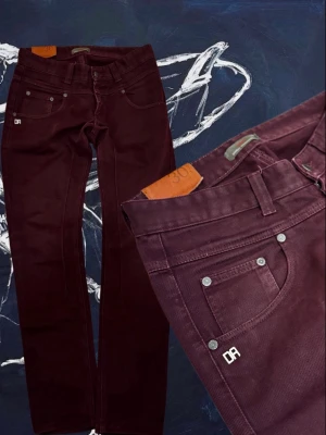 Mörkröda jeans från Daniele Alessandrini🇮🇹 - Säljer ett par mörkröda jeans med raka ben och klassisk femficksmodell. Jeansen har silverfärgade nitar och en liten DR-logga på fickan. Materialet är mjukt och stretchigt för extra komfort. Perfekta för dig som vill ha en snygg och stilren look.