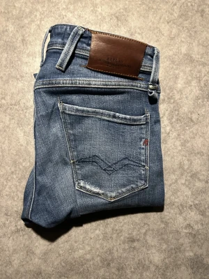 Replay Anbass blå jeans herr - Säljer ett par Replay Anbass jeans i klassisk blå tvätt med slitningar och snygga detaljer på bakfickan. Jeansen har normal passform, fem fickor och är tillverkade i mjuk bomullsdenim med lite stretch för extra komfort. W28 L30