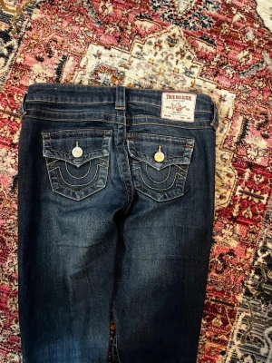 Mörkblå True Religion jeans - Säljer då de inte riktigt passade mig. Fint skick, men har råkat skrapa upp ena knäet samt spillt färg på båda vilket man kan se på sista bilden. Har även lagt upp dem och sedan ner igen vilket man kan se på tredje bilden. Strl 25 