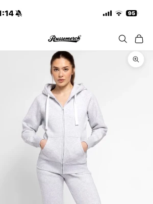 Ljusgrå zip-hoodie från Russermerch - Snygg ljusgrå hoodie med dragkedja från Russermerch. Hoodien har huva med vita snören, två fickor framtill och ribbade muddar vid ärmslut och nederkant. Perfekt för en chill och avslappnad stil.