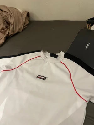 Vit McKenzie t-shirt passar xs-s - Snygg vit t-shirt från McKenzie med svarta paneler längs axlarna och röda sömmar som ger en sportig vibe. Klassisk passform och rund halsringning. Perfekt för en avslappnad stil.