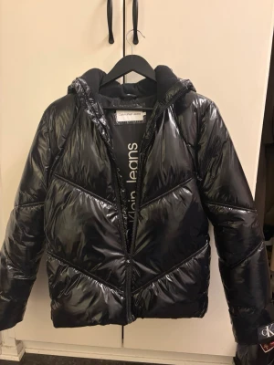 Glansig vinterjacka - Glansig vinterjacka från calvinklein. Jackan köpt från kidsbrandstore och är i storlek 16 men passar som storlek S. Den är i mycket bra skick och bara använd ett fåtal gånger. Luvan är dessutom avtagbar. Superbekväm🥰