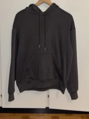 Mörkgrå hoodie med ficka - Säljer en enkel och stilren mörkgrå hoodie i storlek XS. Hoodien har en klassisk känguruficka framtill, dragsko i huvan och ribbade muddar vid ärmar och nederkant. Perfekt för en avslappnad och casual look.