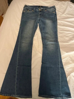 True religon jeans - Säljer ett par true religon jeans med utsvängda ben och klassiska detaljer som fem fickor och gylf med dragkedja och knapp. Jeansen har en snygg tvätt med ljusare partier och är gjorda i jeansmaterial.