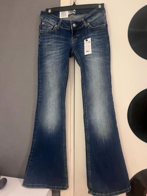 Blå bootcut jeans från Black Soul - Snygga blå bootcut jeans från Black Soul med klassisk femficksmodell och slitningar framtill. Jeansen har låg midja och är tillverkade i ett mjukt jeansmaterial som sitter skönt. Perfekta för dig som gillar en retroinspirerad look.