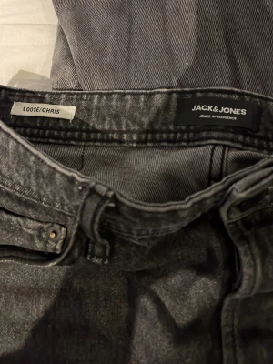 Grå loose fit jeans från Jack & Jones - Säljer ett par grå loose fit jeans från Jack & Jones, modell Chris. Jeansen har en avslappnad passform med raka ben och klassisk femficksdesign. Tillverkade i mjukt denimtyg som ger en skön känsla och cool look.