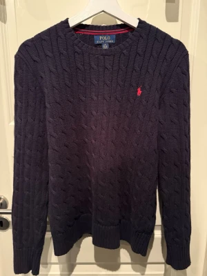 Mörkblå kabelstickad tröja Polo Ralph Lauren - Mörkblå kabelstickad tröja från Polo Ralph Lauren i stl 14-16 år. Pris kan diskuteras 