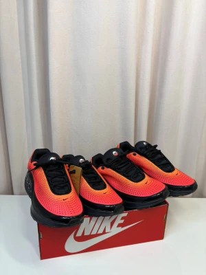 Nike Air Max ”DN” - Nike sneakers med futuristisk design i röd och svart mesh. Skorna har en chunky svart sula med synliga luftbubblor på sidan, svarta snören och små swoosh-loggor. Ovandelen är ventilerad och har en snygg gradient från rött till orange. Perfekta för dig som vill sticka ut. 2 par för priset av 1