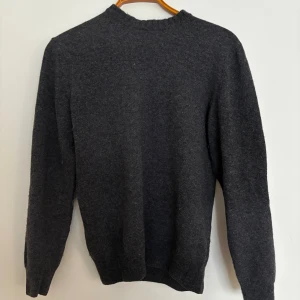 Mörkgrå stickad tröja med armbågslappar - Mysig mörkgrå stickad tröja med ljusgrå armbågslappar. Tröjan har rund halsringning, långa ärmar och ribbade muddar vid ärmslut och nederkant. Perfekt för kalla dagar och enkel att matcha med jeans eller kjol.