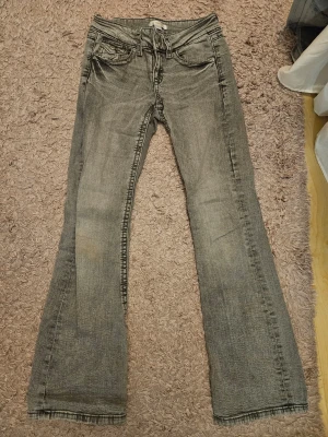 Bootcut jeans från Gina Tricot, grå - Jag säljer ett par ljusgrå jeans från Gina Tricot i storlek 152. Modellen har låg midja, bootcut-ben, klassiska fem fickor och snygga detaljer på bakfickorna. Jeansen är använda ett fåtal gånger och har därför inga skador förutom ett litet hål som tyvärr blev i en av bakfickorna vid tidig användning, men som jag har sytt ihop själv så att det nu ser ut som en fin detalj istället, och en svag fläck på ena känt. (Se bilder) Nypris runt 300 kr. 