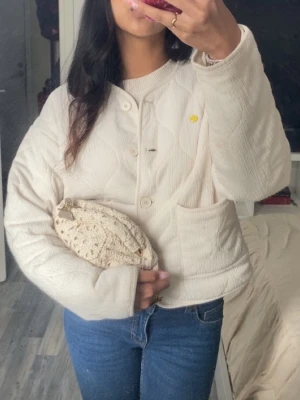 Quiltad beige jacka från Gina Tricot - Superfin quiltad jacka i beige från Gina Tricot. Jackan har rund hals, stora fickor framtill och stängs med knappar. Den är lätt oversized och har ett mjukt, strukturerat tyg som ger en chill vibe. Perfekt att slänga på sig över en hoodie eller t-shirt. Slutsåld överallt!