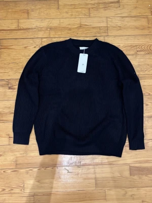 mörk blå stickad tröja Maison Margiela - Säljer en svart ribbstickad tröja från Maison Margiela i storlek M. Tröjan har klassisk rund halsringning, långa ärmar och de ikoniska vita sömmarna i nacken. Perfekt till lager på lager under höst och vinter.
