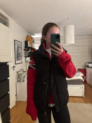 Svart dunväst från Bershka - Svart dunväst från Bershka med hög krage och dragkedja framtill. Västen är quiltad och har en enkel, stilren design som passar perfekt över en hoodie eller tröja. Tillverkad i syntetmaterial och ger en cool och avslappnad look.