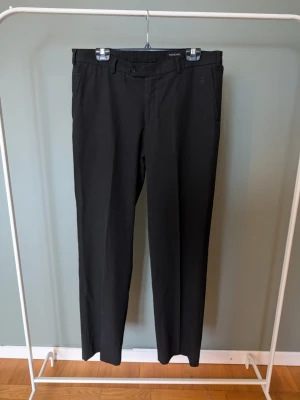 Svarta kostymbyxor från Douglass - Säljer ett par klassiska svarta kostymbyxor från Douglass. Byxorna har raka ben, bälteshällor och diskreta fickor både fram och bak. Perfekta till skjorta eller stickad tröja. Materialet känns mjukt och har en snygg, matt finish.