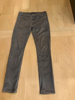 Grå jeans från Nudie Jeans  - Passar 32/34. Säljer ett par grå jeans från Nudie Jeans Co med klassisk femficksdesign och dragkedja i gylfen. Jeansen har raka ben och subtila detaljer på bakfickan. Materialet är mjukt denim i bomull och passformen är normal.
