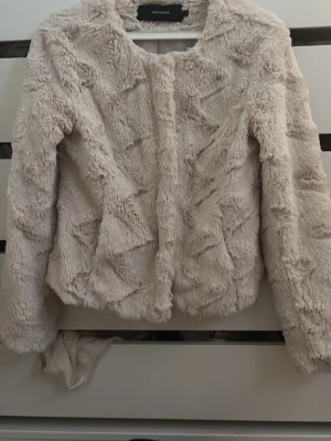 Beige pälsjacka från Vero Moda XS - Säljer en fluffig och supermjuk beige pälsjacka från Vero Moda i storlek XS. Jackan har rund halsringning, långa ärmar och stängs med tryckknappar framtill. Perfekt för dig som vill ha en cozy look med lite extra attityd.