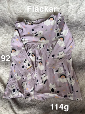 Lila kattklänning med regnbågar - Supersöt lila klänning med lång ärm och gulligt kattmönster, regnbågar och små hjärtan. perfekt för dig som gillar färgglada prints och lekfull stil.🌸 Fläckar. Storlek 92