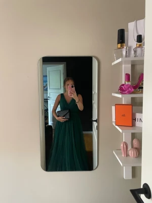 Balklänning  - Säljer en elegant långklänning i djupgrönt med v-ringad omlott-topp och ärmlös design. Klänningen har ett luftigt, lager-på-lager tyg i tunn polyester som ger ett svepande intryck. Perfekt för bal eller student! 💚